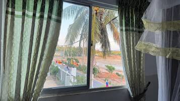 A window with curtains, a view of palm trees, and a flag.