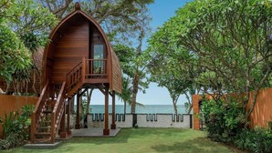 Une cabane en bois perchée dans un arbre, dotée d’un balcon, entourée d’une végétation luxuriante et offrant une vue sur la mer.
