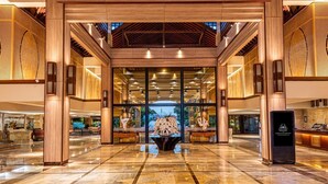 Un hall d’entrée spacieux avec un plafond haut, des poutres en bois et une composition florale centrale.