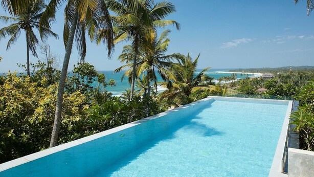Una piscina infinita de color azul claro con vistas al océano y palmeras.