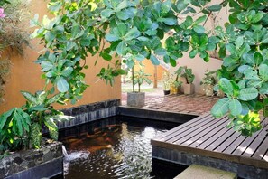Un jardín tranquilo con un pequeño estanque, rodeado de abundante vegetación y plantas en macetas.