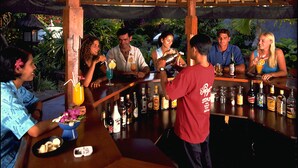 A bar area with wooden beams and a thatched roof, surrounded by greenery. - Poppies Bali (Kuta)