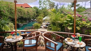 An outdoor dining area with tables and chairs, a pool, and lush greenery. - Poppies Bali (Kuta)