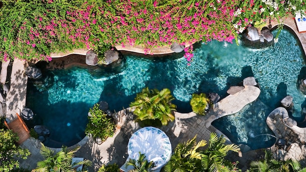 An aerial view of a pool area with multiple water features, surrounded by lush greenery and pink flowers. - Poppies Bali (Kuta)