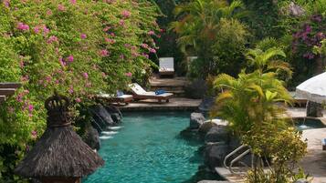 A tropical resort with a clear pool, lounge chairs, and lush greenery.