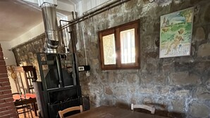 Un coin repas rustique avec une table et des chaises en bois, un mur en pierre et un poêle d’époque.