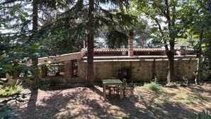 Un bâtiment rustique en pierre, doté d’un toit en tuiles, entouré d’arbres et agrémenté d’une petite table avec des chaises.