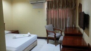 Una habitación de hotel con una cama, una silla, un escritorio, aire acondicionado y una televisión.
