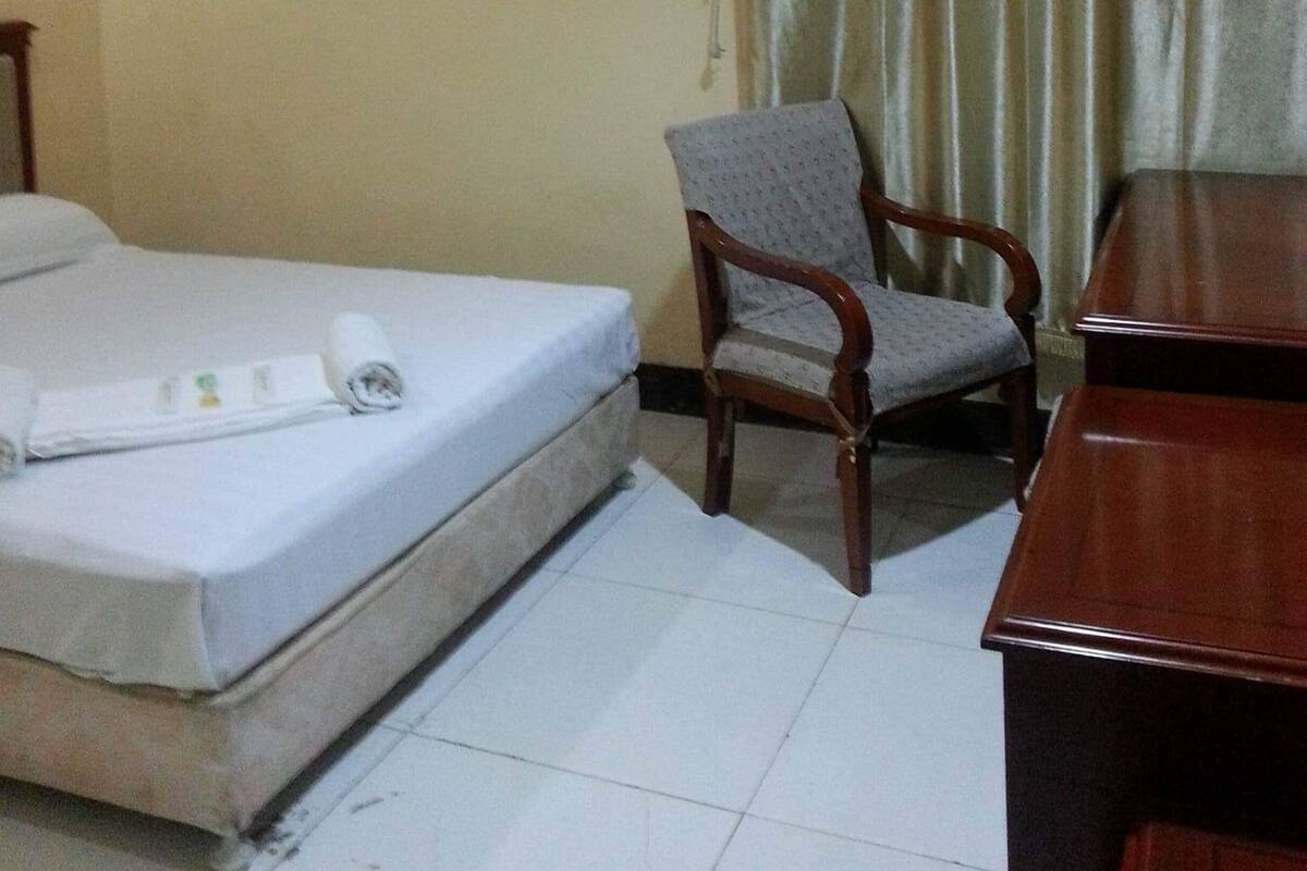 Ein Hotelzimmer mit Bett, Sessel, Schreibtisch und Klimaanlage an der Wand.