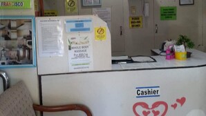 Un mostrador de recepción con un cartel que dice 'Cajero', una silla y varios carteles informativos en la pared.