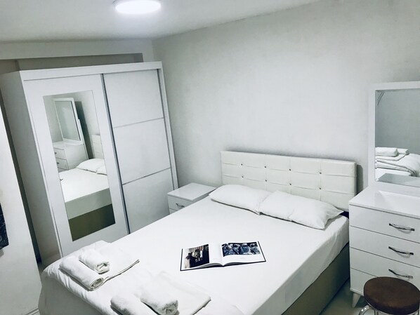 A bedroom with a bed, a bedside table, a mirror, a wardrobe, and a small stool. - Istanbul Harmony Hostel (Istanbul)