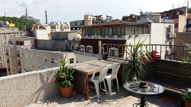 A rooftop terrace with a table and chairs, potted plants, and a view of surrounding buildings. - Istanbul Harmony Hostel (Istanbul)