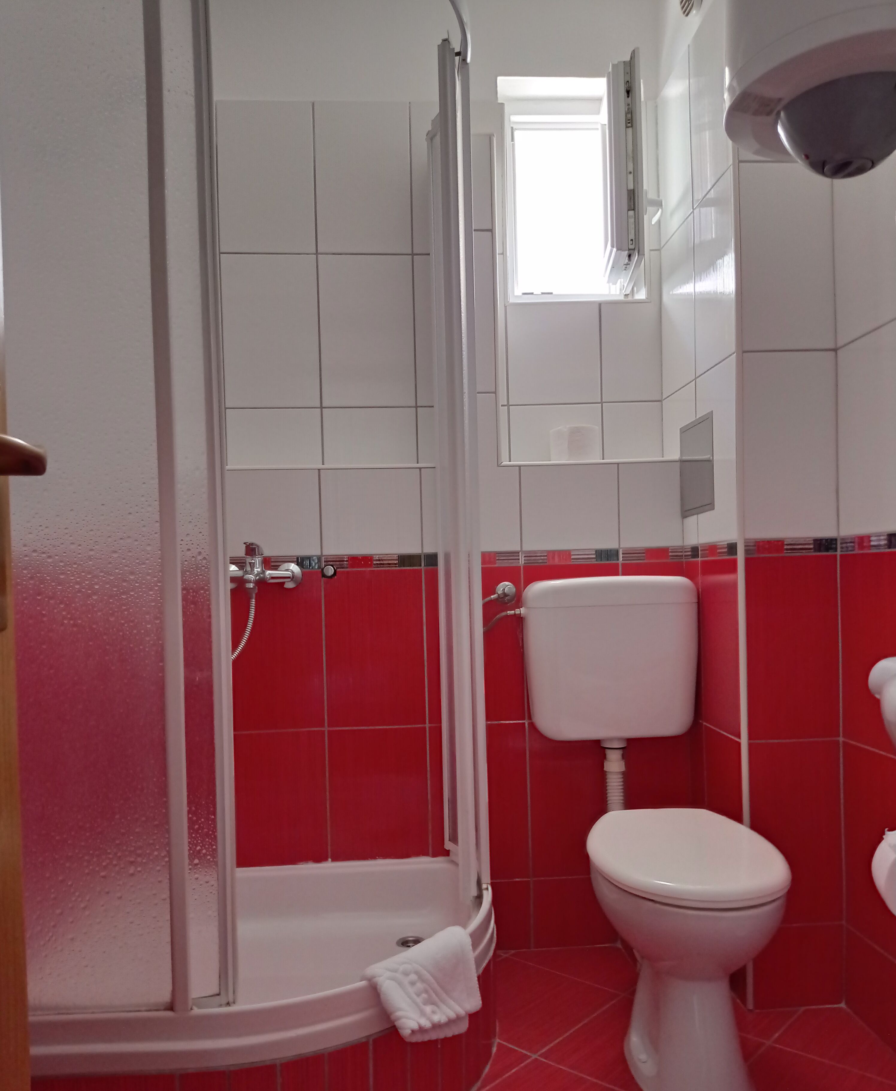 Et badeværelse med brusebad, toilet og et vindue.
