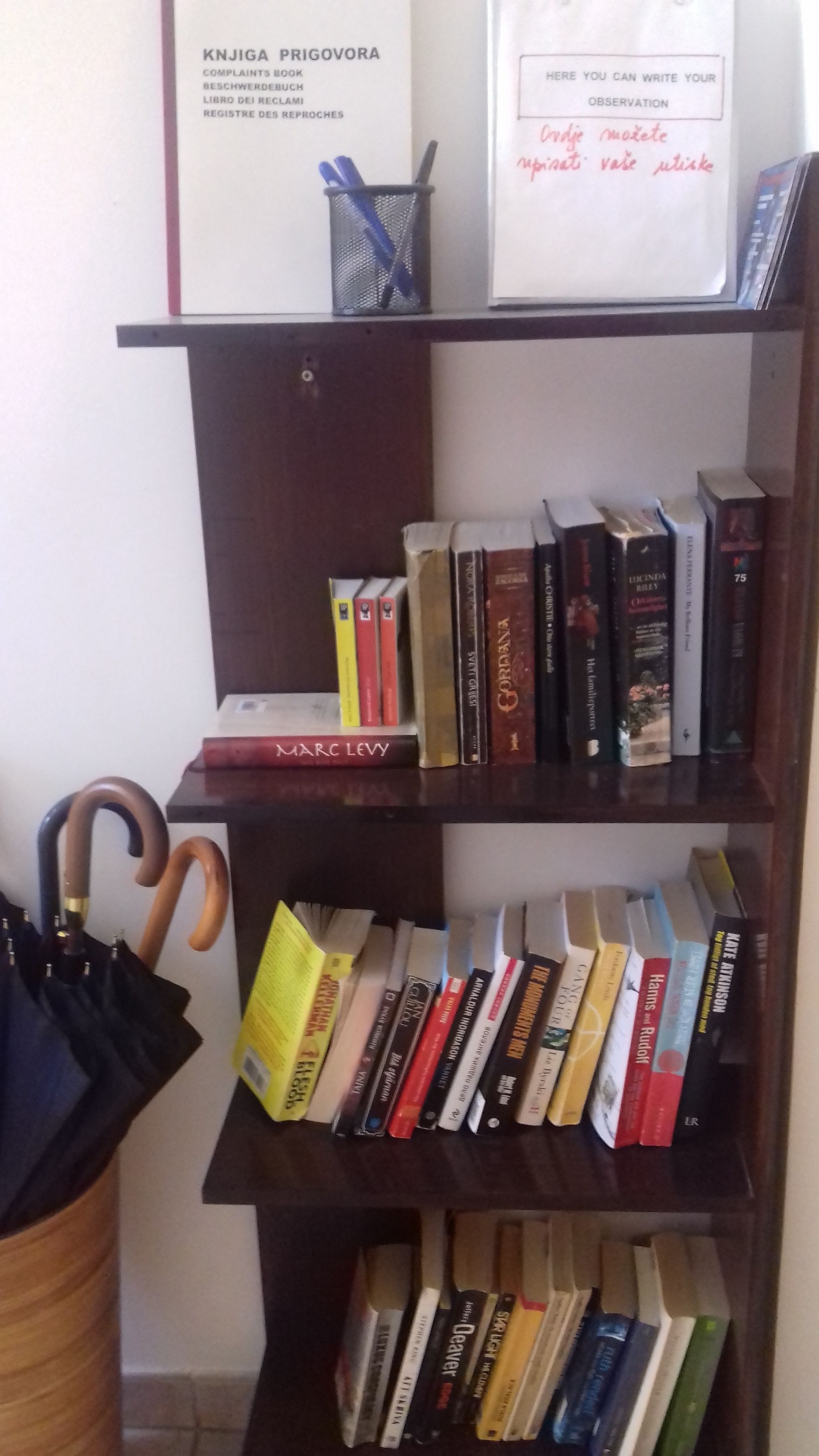 A bookshelf with various books, a pen holder, and a cane.
