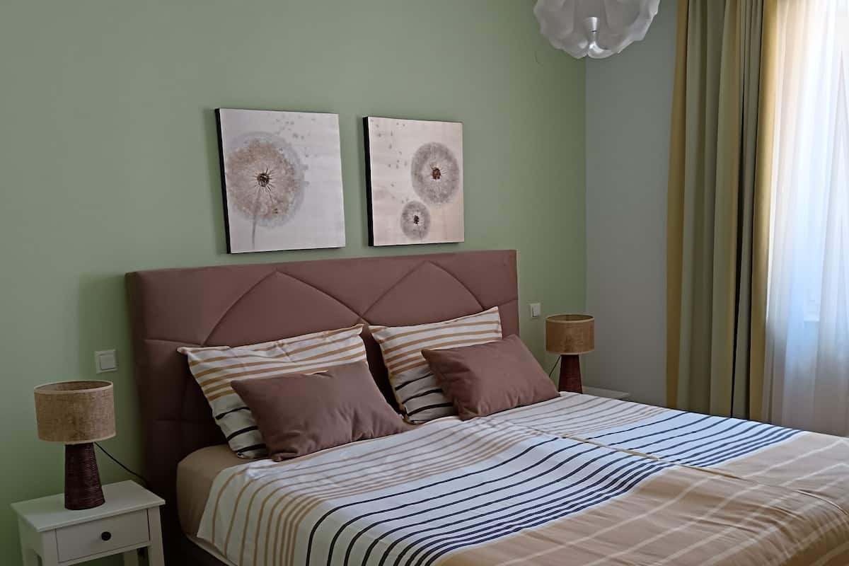 A bedroom with a bed, two wall art pieces, a lamp, and a window with curtains.