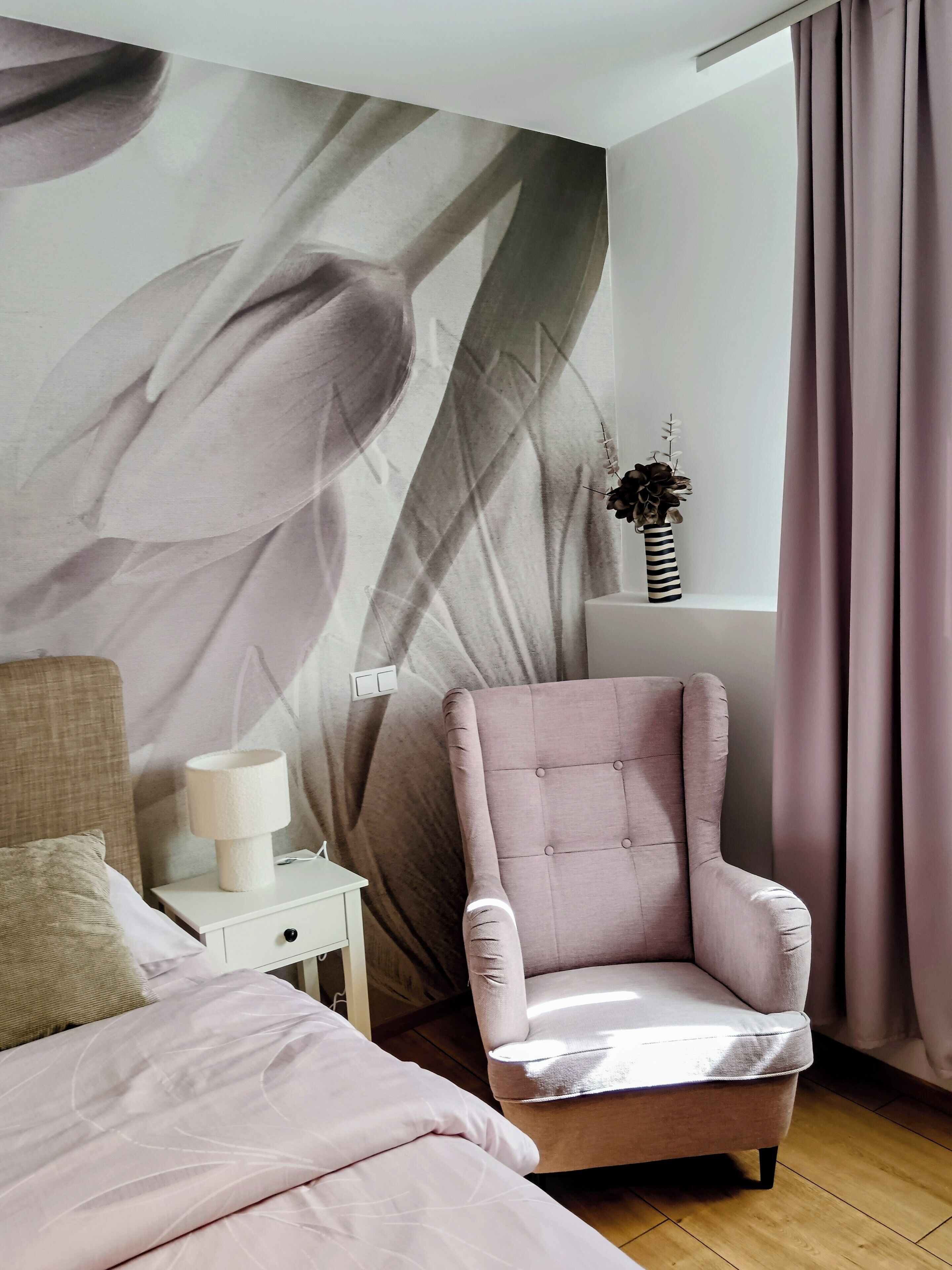 A bedroom with a bed, a chair, a nightstand, a lamp, and a wall with a leaf pattern.