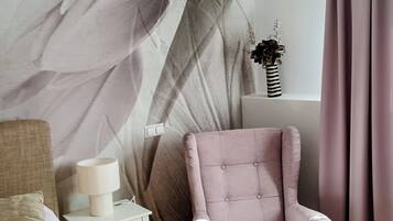 Un dormitorio con una cama, una silla, una mesita de noche, una lámpara y una pared con diseño de hojas.