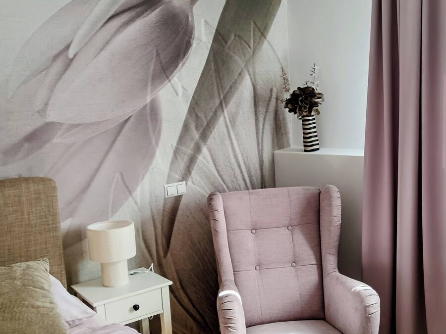 Un dormitorio con una cama, una silla, una mesita de noche, una lámpara y una pared con diseño de hojas.