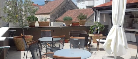 An outdoor patio with wicker chairs and tables, potted plants, and a white umbrella.