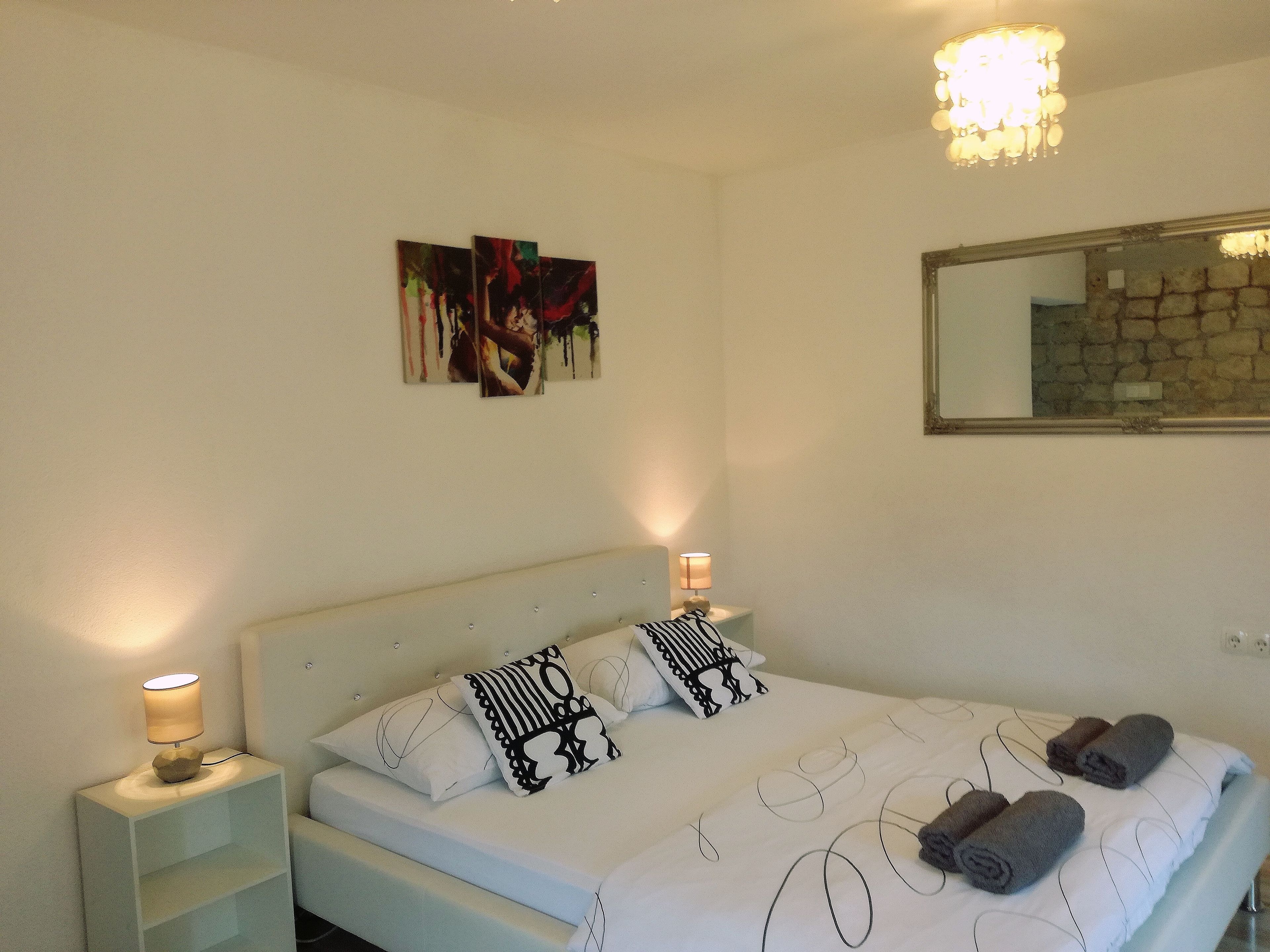 A bedroom with a bed, two bedside lamps, a nightstand, and a wall-mounted painting.