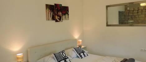 A bedroom with a bed, two bedside lamps, a nightstand, and a wall-mounted painting.