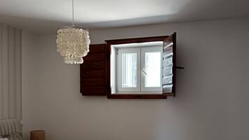 Un dormitorio con cama, una silla, una mesita, una ventana con cortinas y un candelabro.