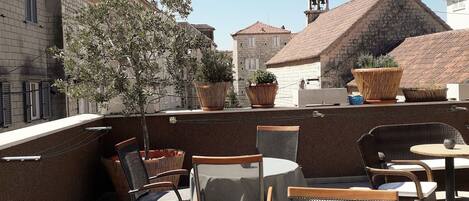 An outdoor seating area with wicker chairs and a round table, surrounded by stone walls and potted plants.
