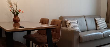 A modern living room with a dining area, featuring a sofa, chairs, a table, and a decorative vase.