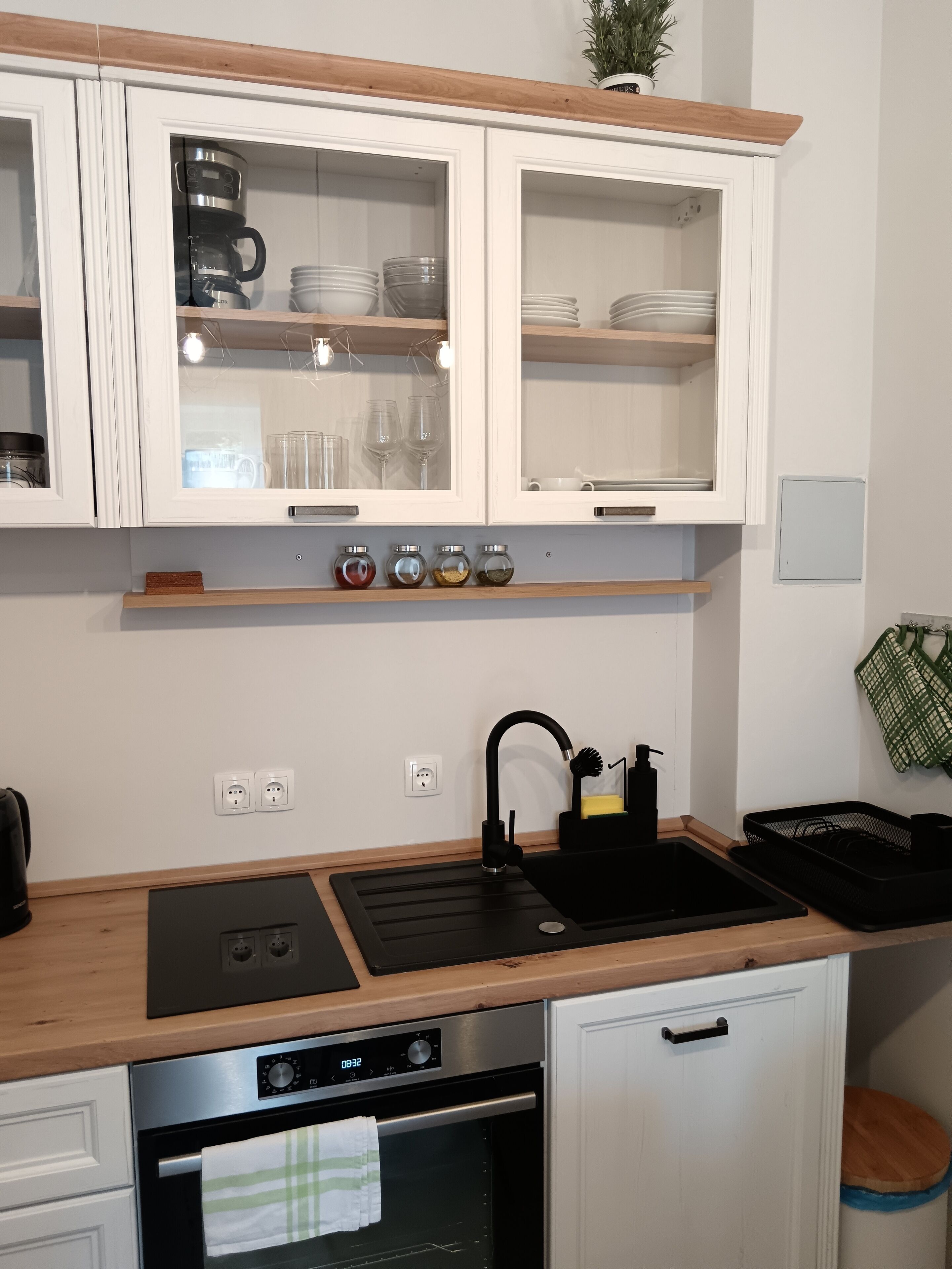 A compact kitchen with white cabinets, a built-in coffee maker, a sink, and an oven.