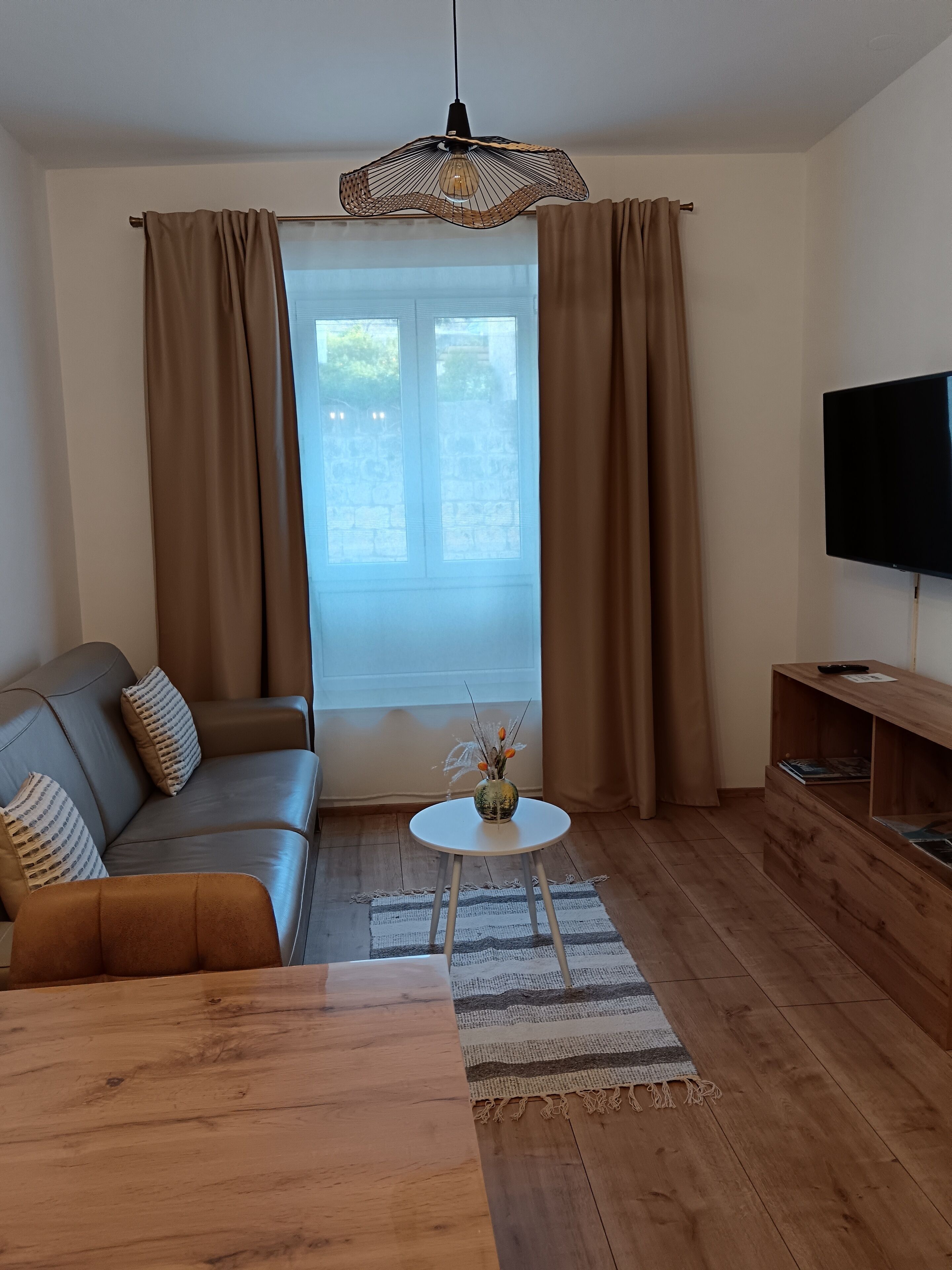 Un salon moderne avec un canapé, une table basse, un téléviseur et une grande fenêtre avec des rideaux.