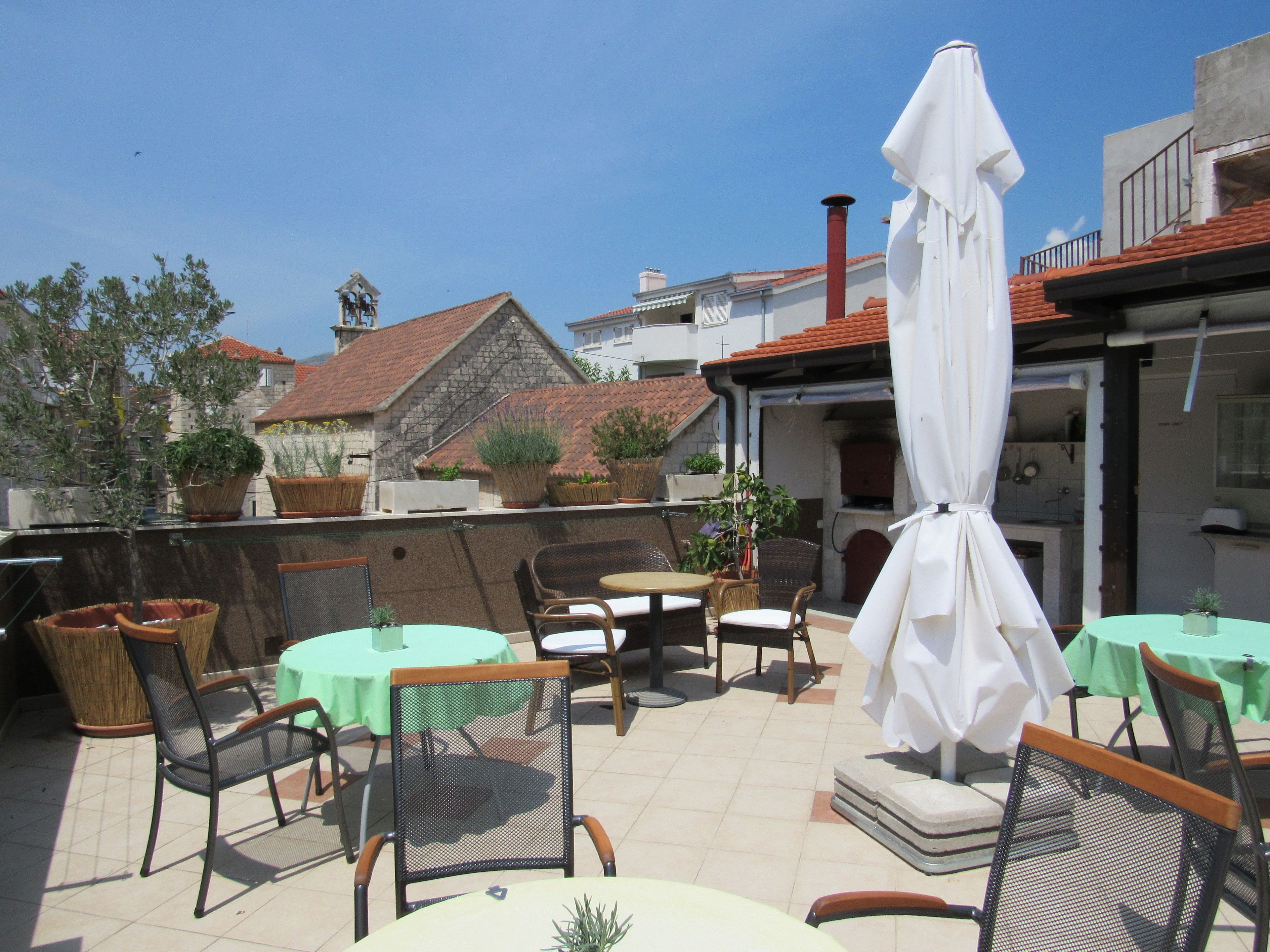 An outdoor patio with tables and chairs, surrounded by potted plants and a white umbrella.