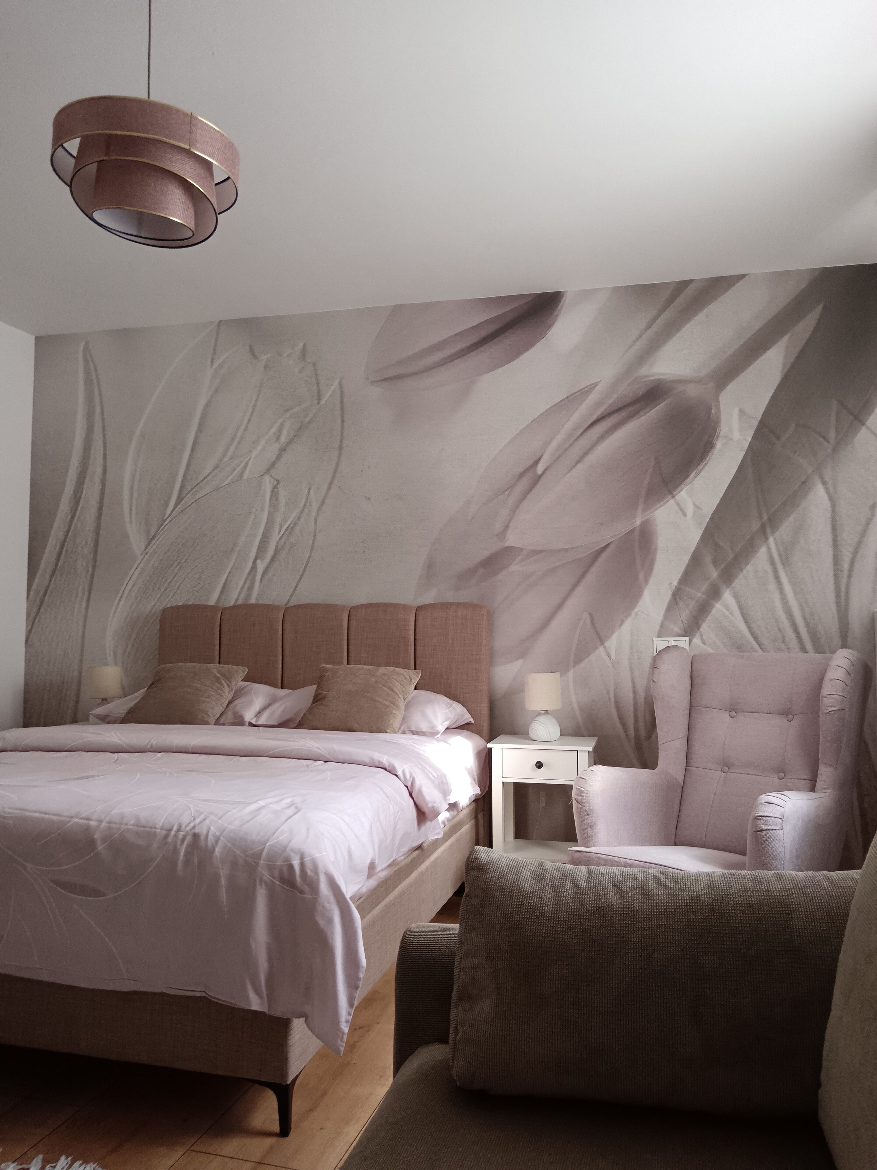 A bedroom with a bed, nightstand, chair, and a wall mural.