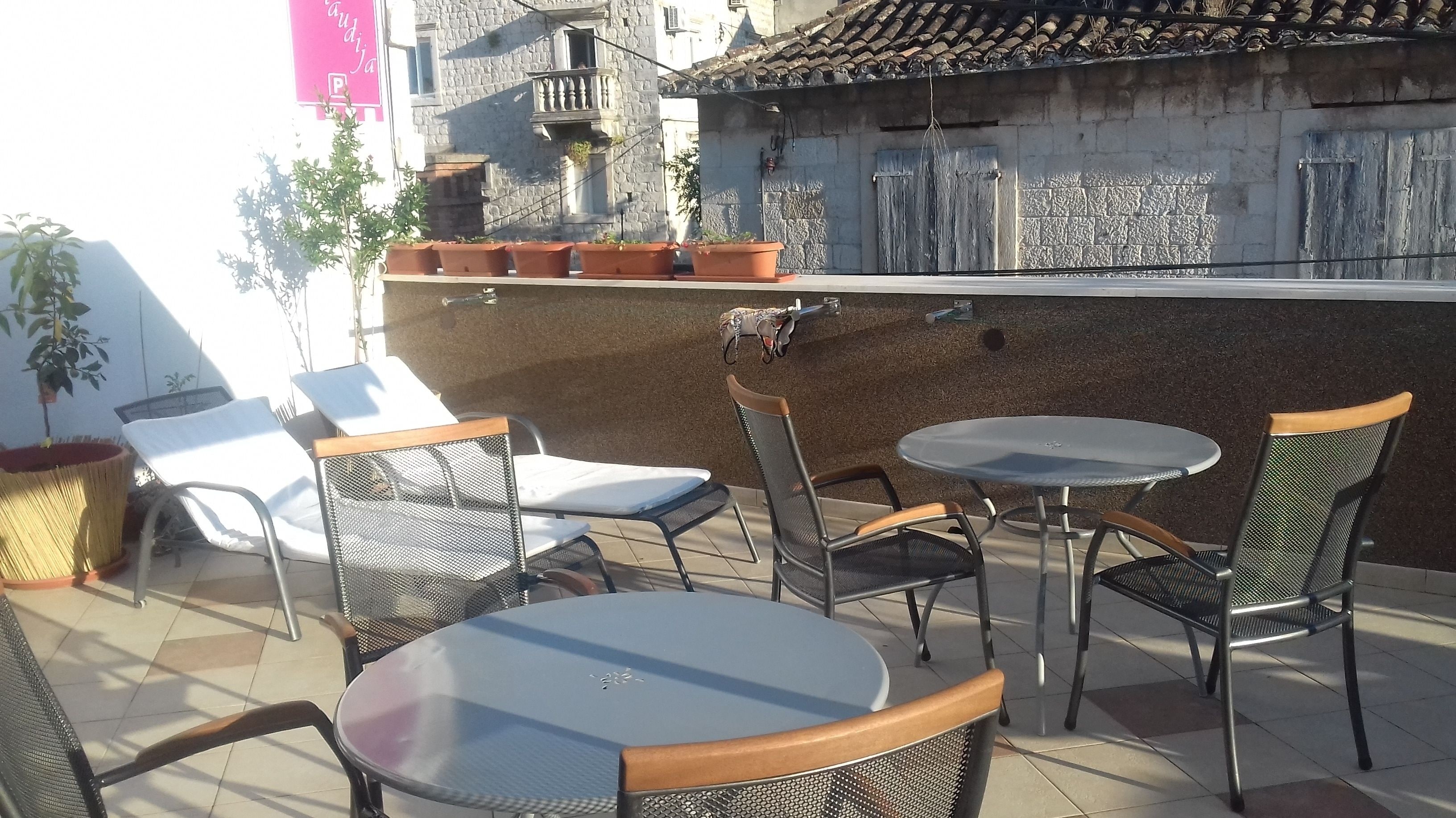 Un patio al aire libre con mesas y sillas redondas, plantas en macetas y una pared de piedra.