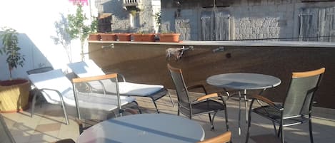 Un patio al aire libre con mesas y sillas redondas, plantas en macetas y una pared de piedra.