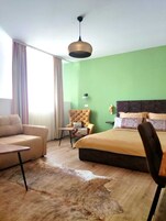 A bedroom with a bed, a sofa, a chair, a small table, and a hanging light fixture.