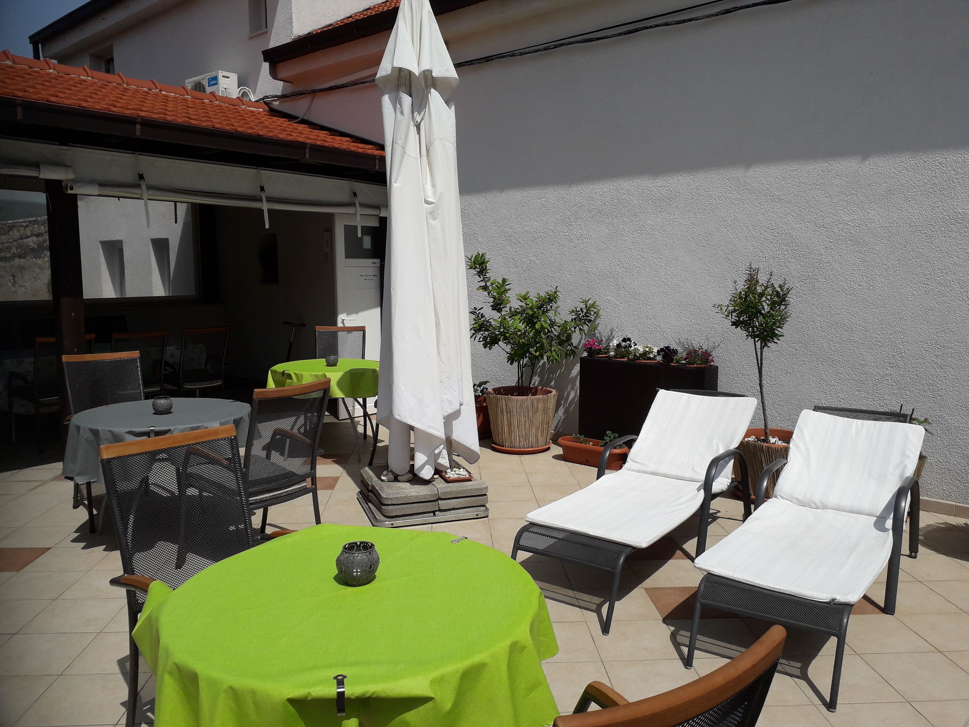 An outdoor patio with a round table, chairs, a white umbrella, and lounge chairs.