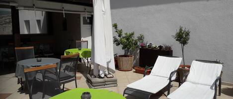 An outdoor patio with a round table, chairs, a white umbrella, and lounge chairs.