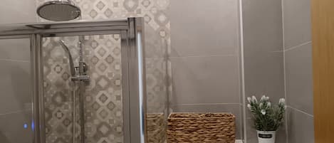 Un baño moderno con ducha acristalada, lavamanos integrado y un estante pequeño con una planta en maceta.
