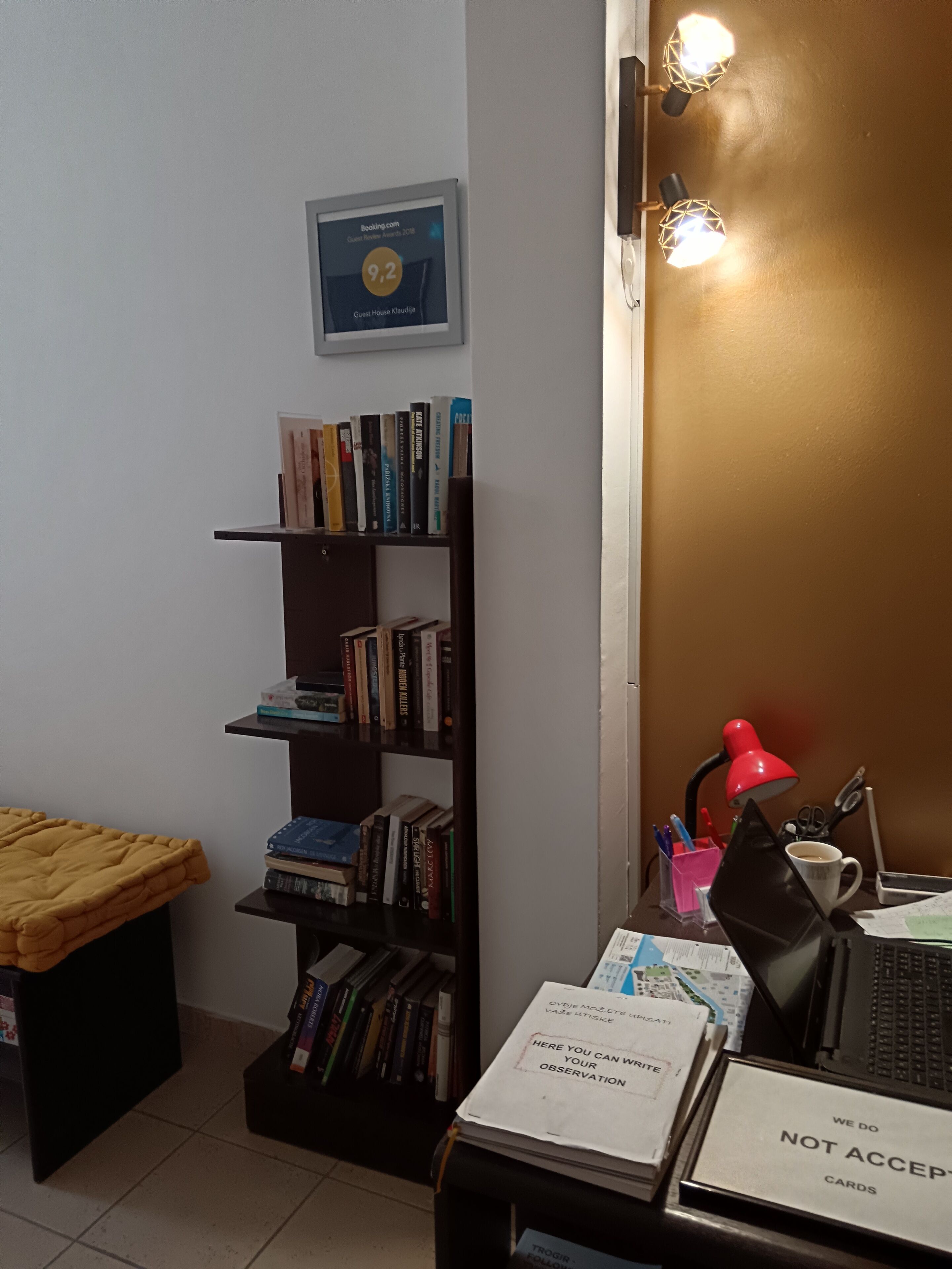 Et værelse med en reol, et skrivebord med en bærbar computer, en rød lampe og et skilt med teksten 'Accepterer ikke kort'.