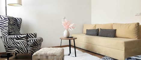 A modern living room with a zebra-striped chair, a beige sofa with patterned pillows, a small round table with a vase, and a floor lamp.
