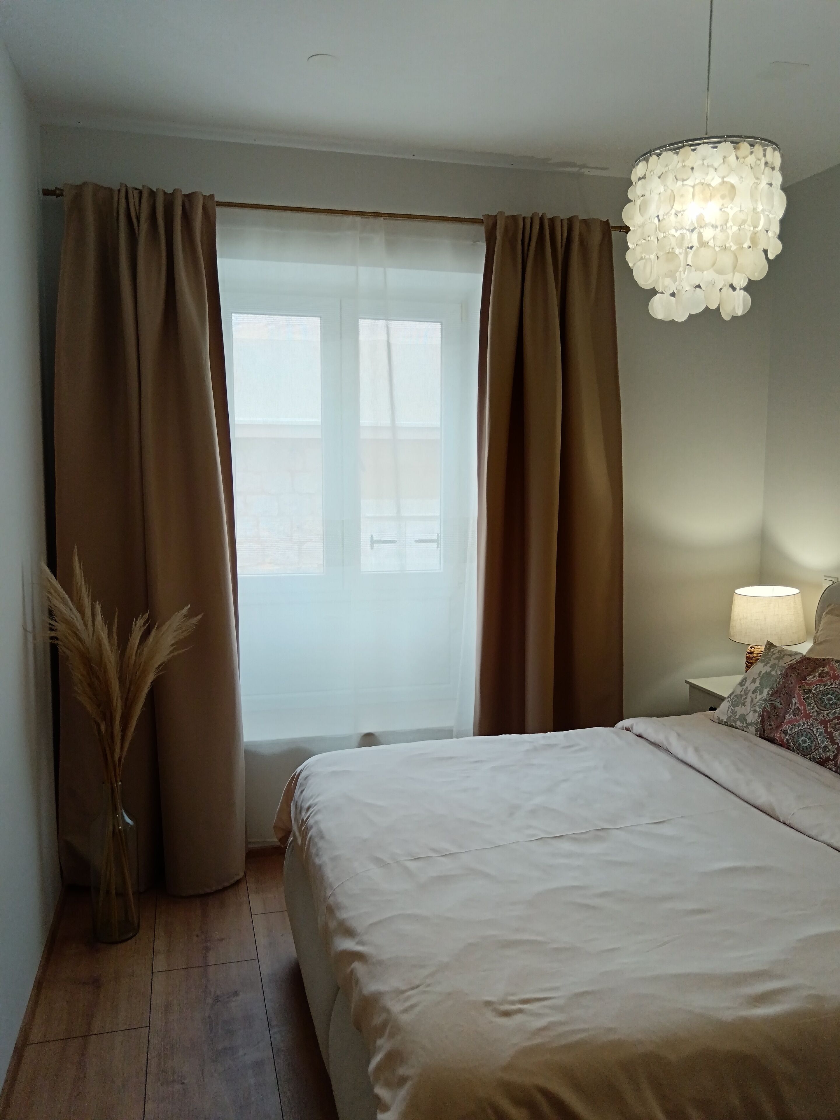A bedroom with a bed, a window with curtains, a bedside lamp, and a decorative light fixture.