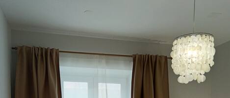 A bedroom with a bed, a window with curtains, a bedside lamp, and a decorative light fixture.