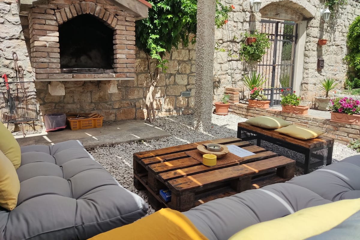 An outdoor seating area with a stone wall, a brick oven, and potted plants.