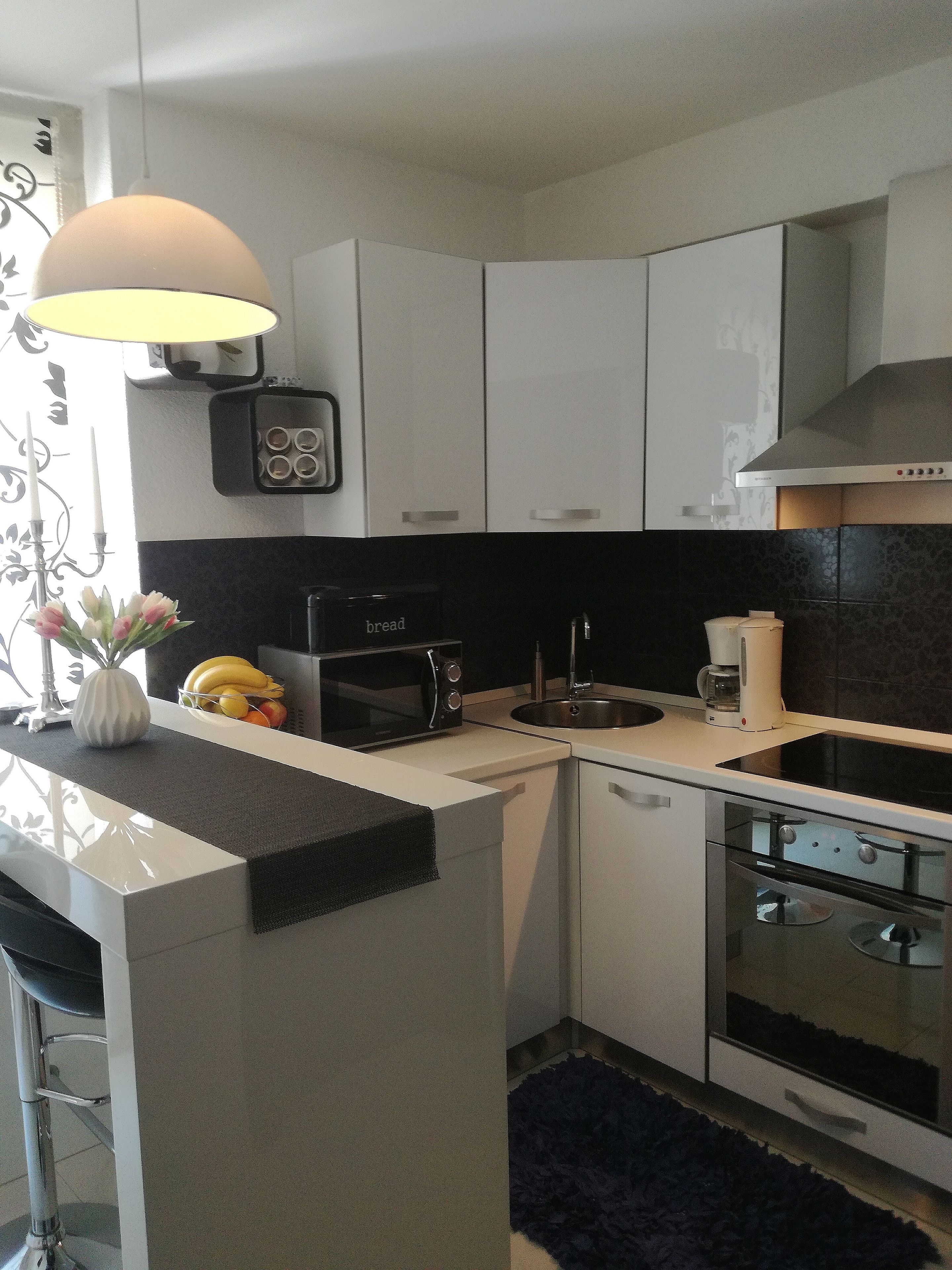 A modern kitchen with white cabinets, a black countertop, a microwave, a stove, and a sink.