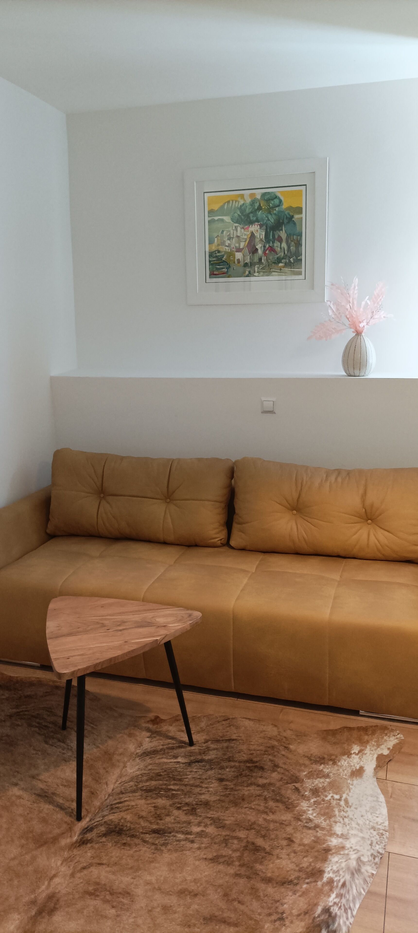 Een woonkamer met een beige bank, een klein houten tafeltje en een pluizig vloerkleed.