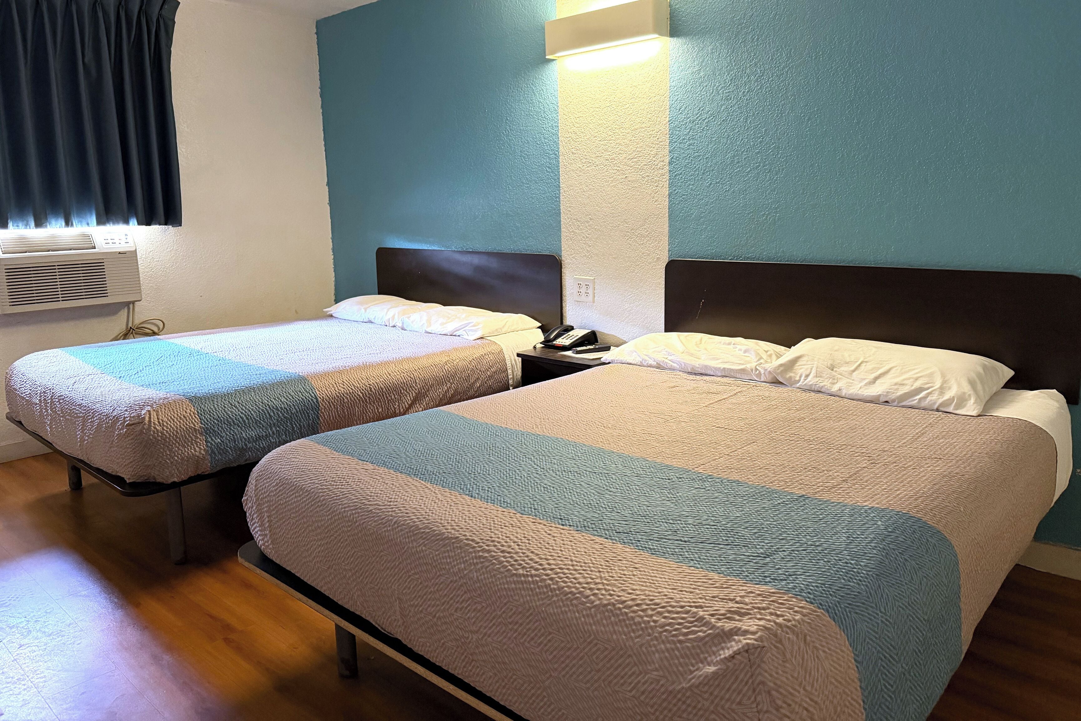 A hotel room with two beds, a wall-mounted air conditioner, and a bedside table with a phone.