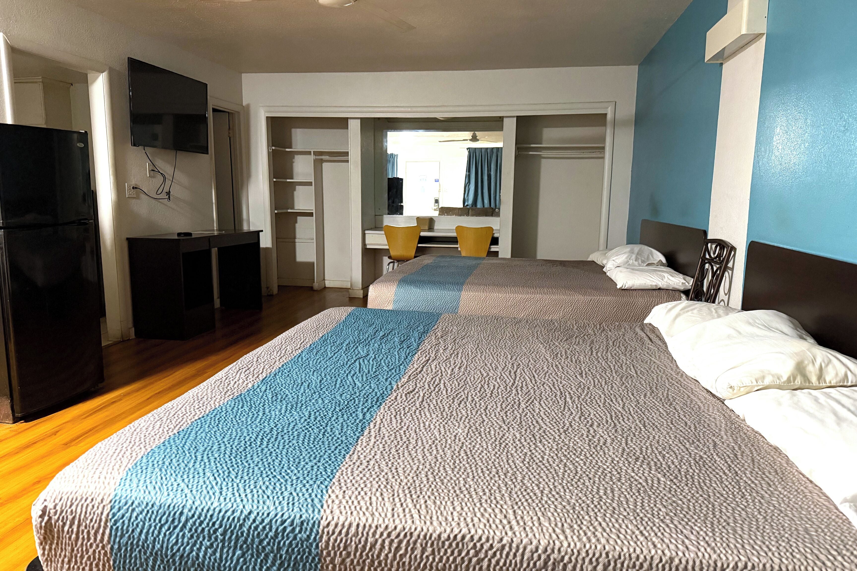 A hotel room with a large bed, a desk with a chair, a television mounted on the wall, and a refrigerator.
