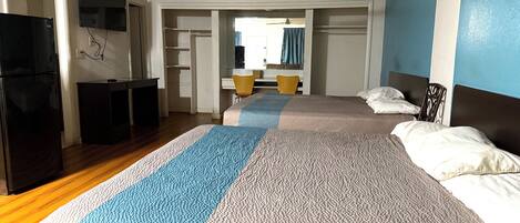 A hotel room with a large bed, a desk with a chair, a television mounted on the wall, and a refrigerator.