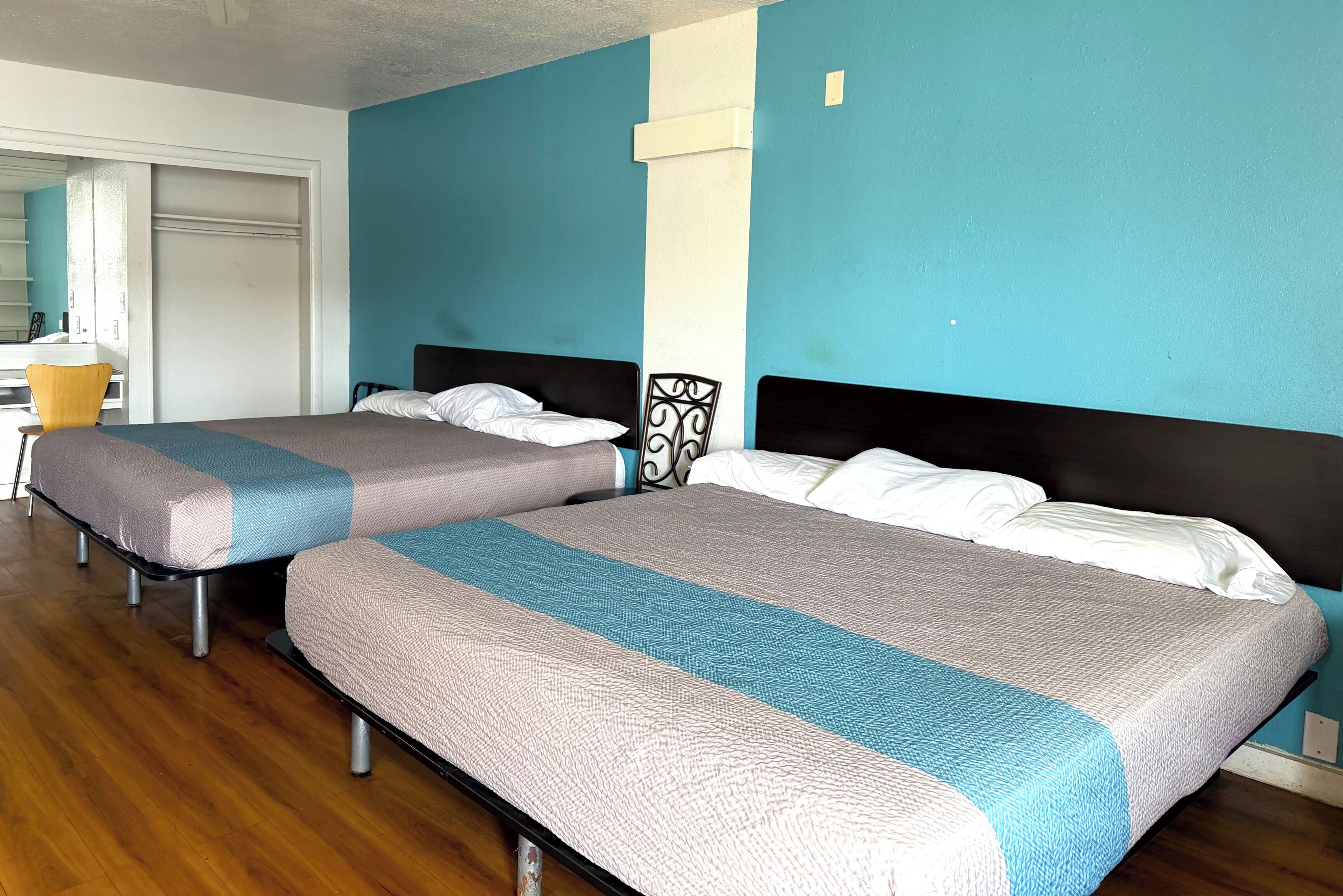 A hotel room with two beds, wooden flooring, and a blue accent wall.