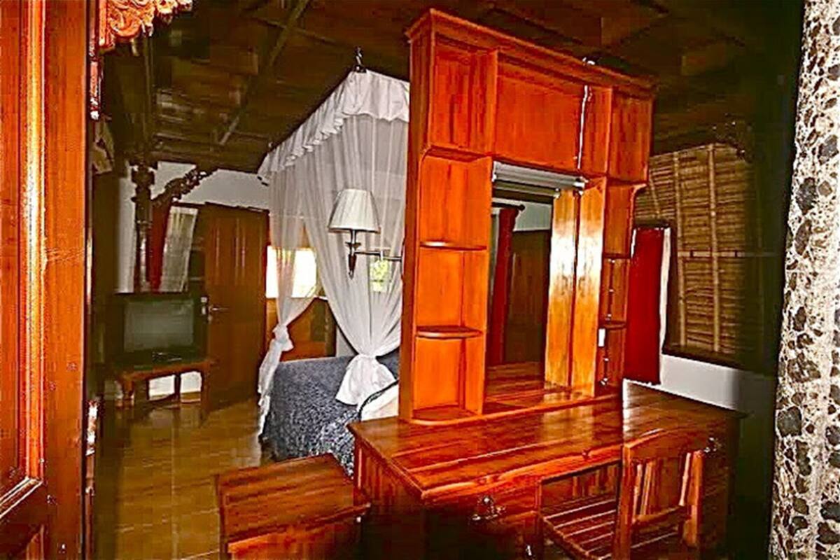 Una habitación con una cama de madera, televisión y ventana con cortinas.